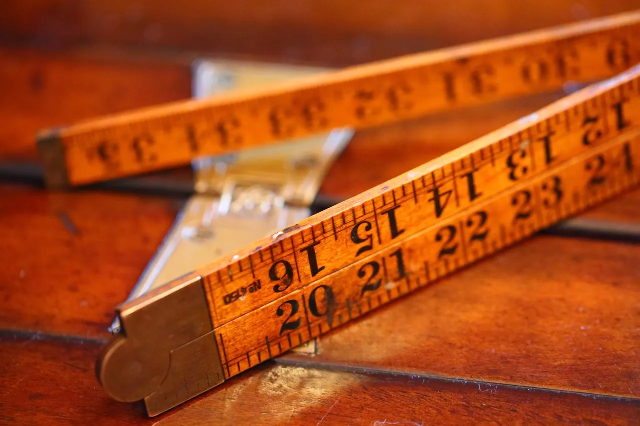 A folding wooden ruler and a metal tape measure lying on a wooden table