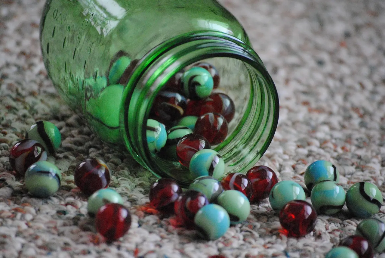 A glass jar tipped on its side with marbles spilling out across a pale floor