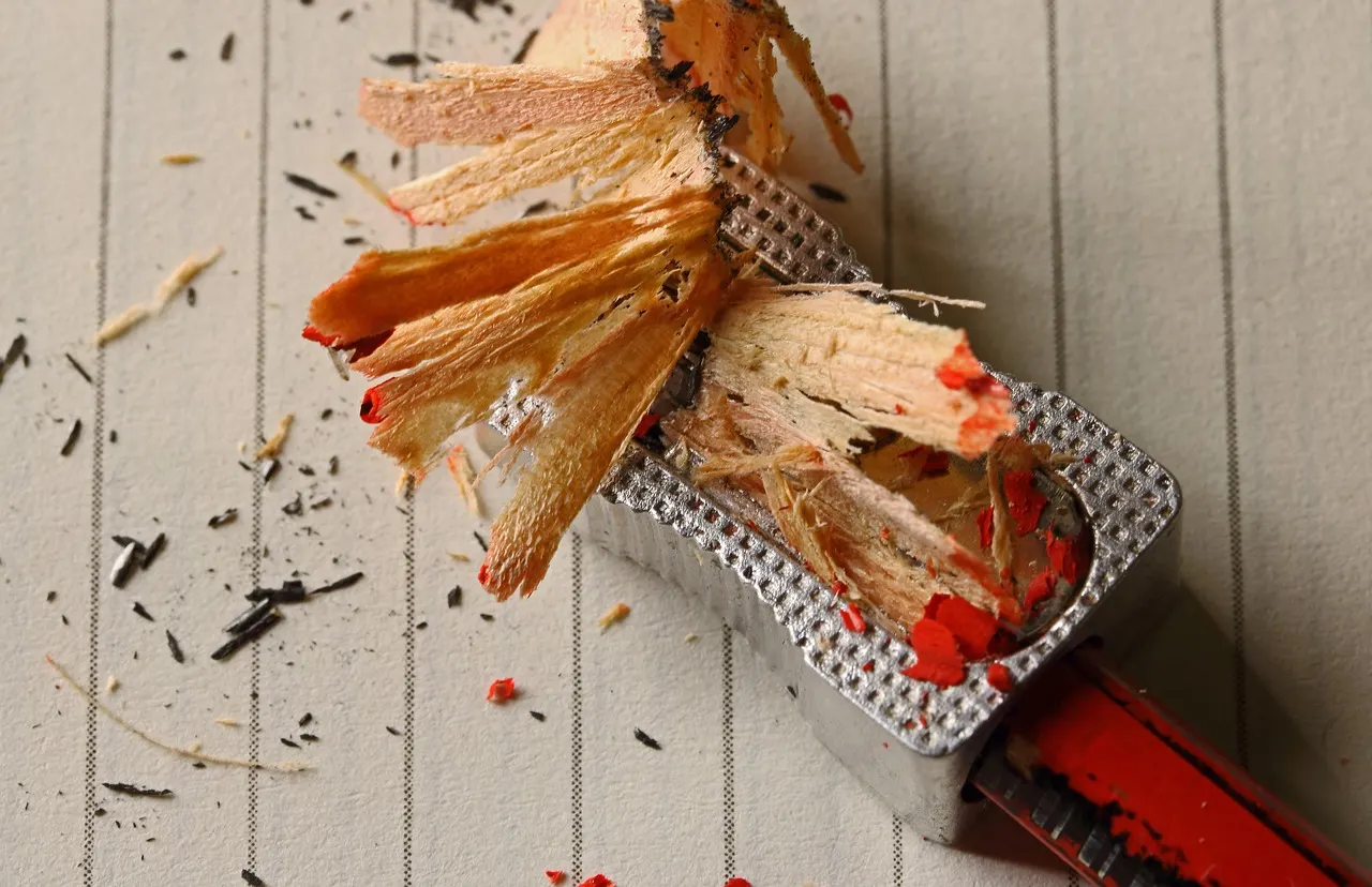 A metal pencil sharpener with a curl of fresh shavings on a pale wooden desk