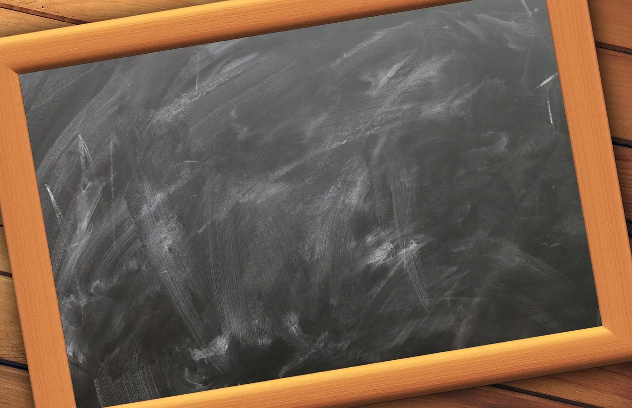 An empty slate blackboard in a wooden frame, chalk dust smeared across it