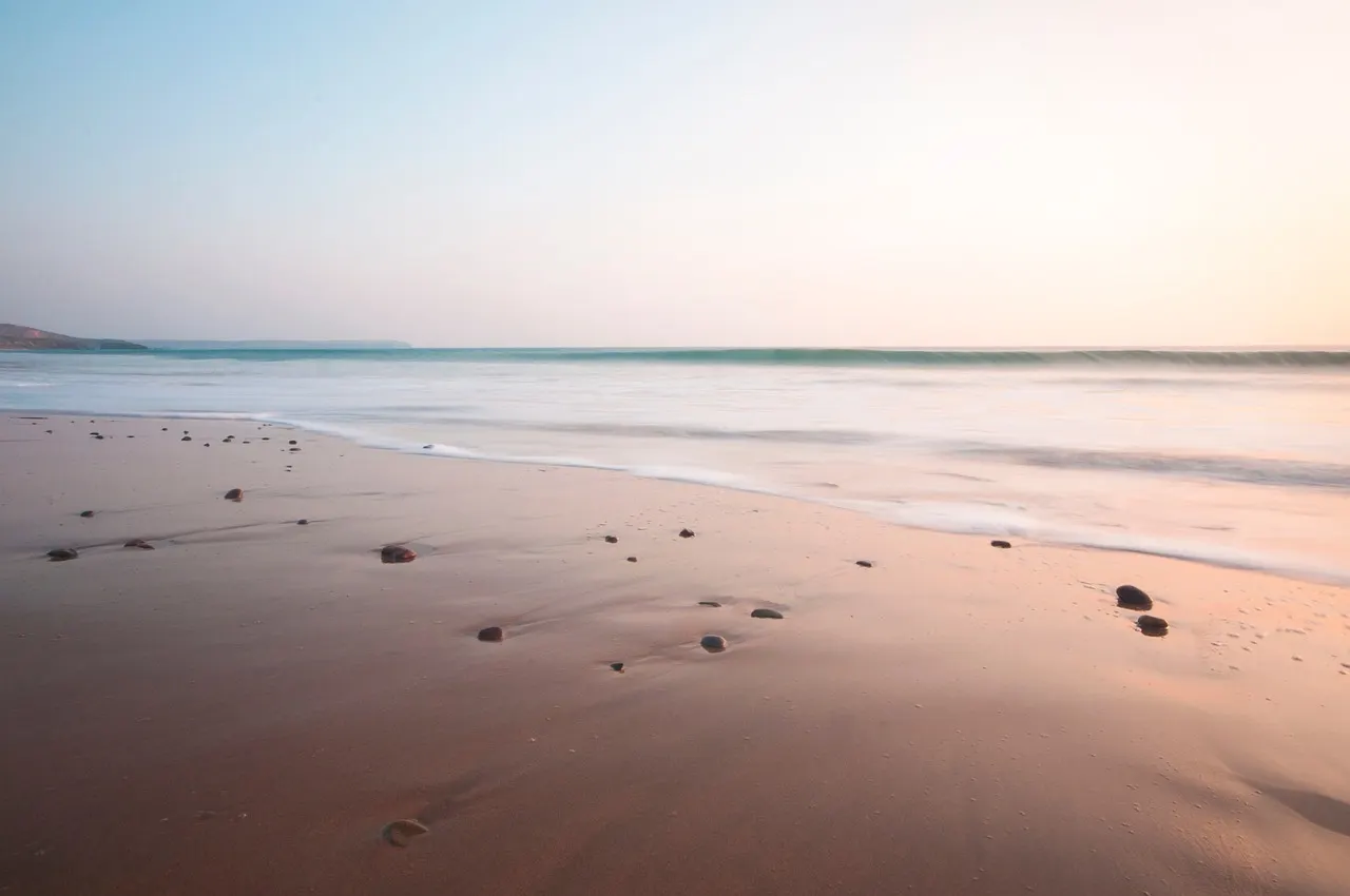 A line of footprints in wet sand curving away along the shoreline