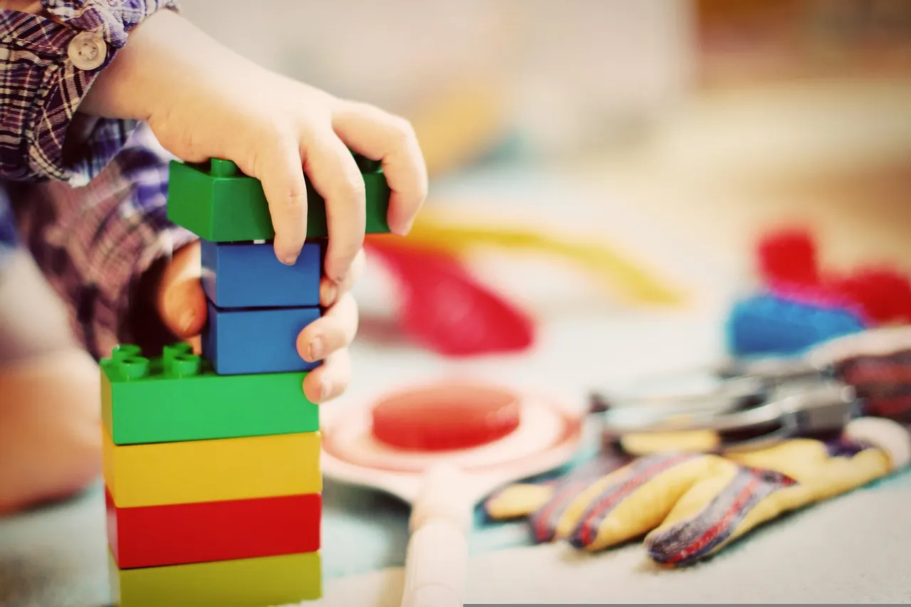 A child's hands stacking building blocks into a tower on a table