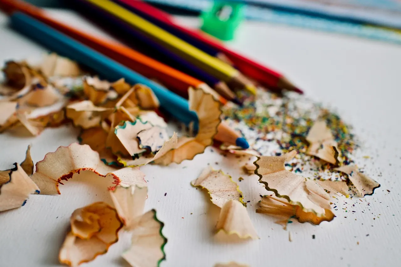 Colored pencils lying beside a curl of pencil shavings on white paper