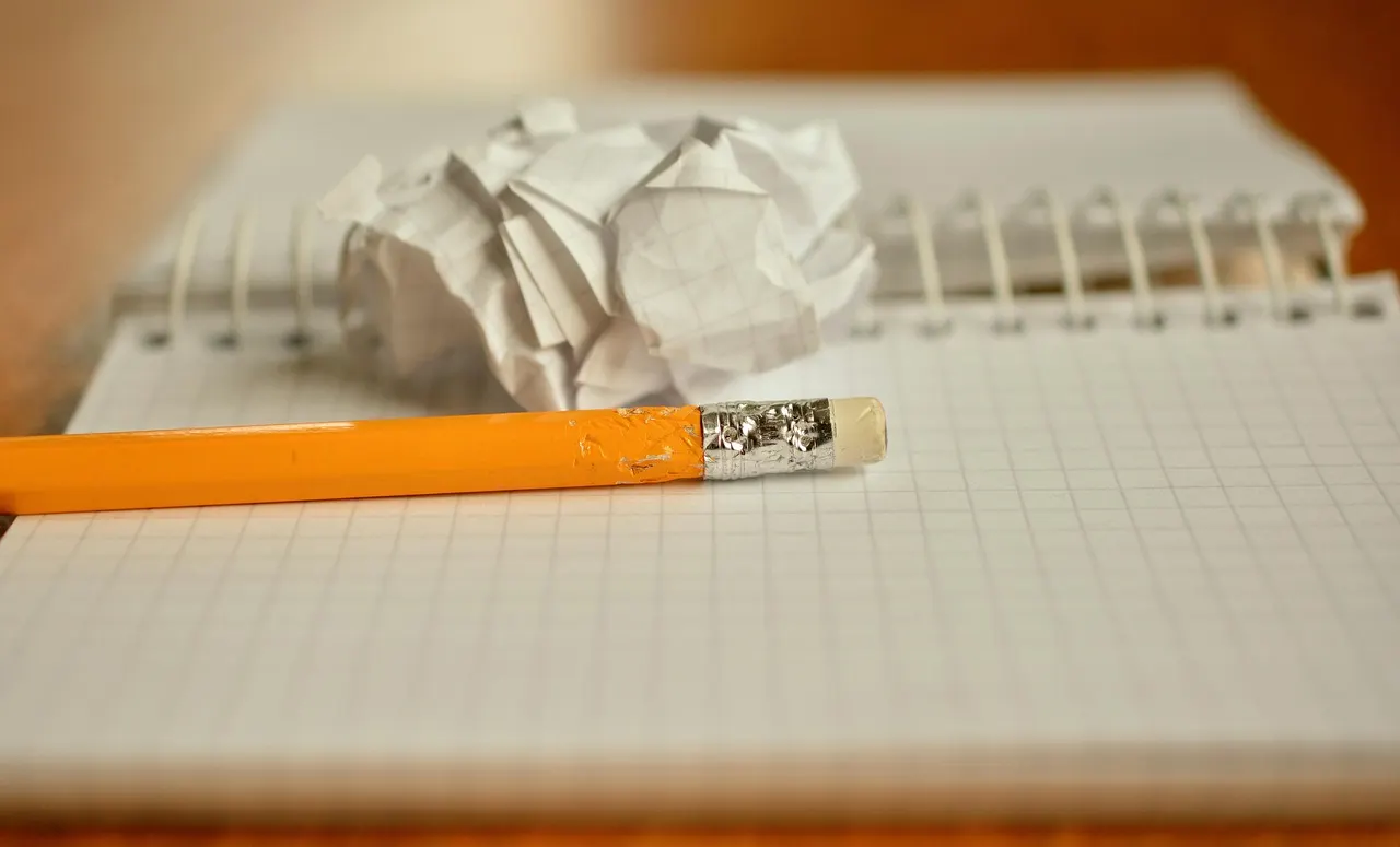 A pencil resting on a spiral notebook beside a crumpled sheet of paper