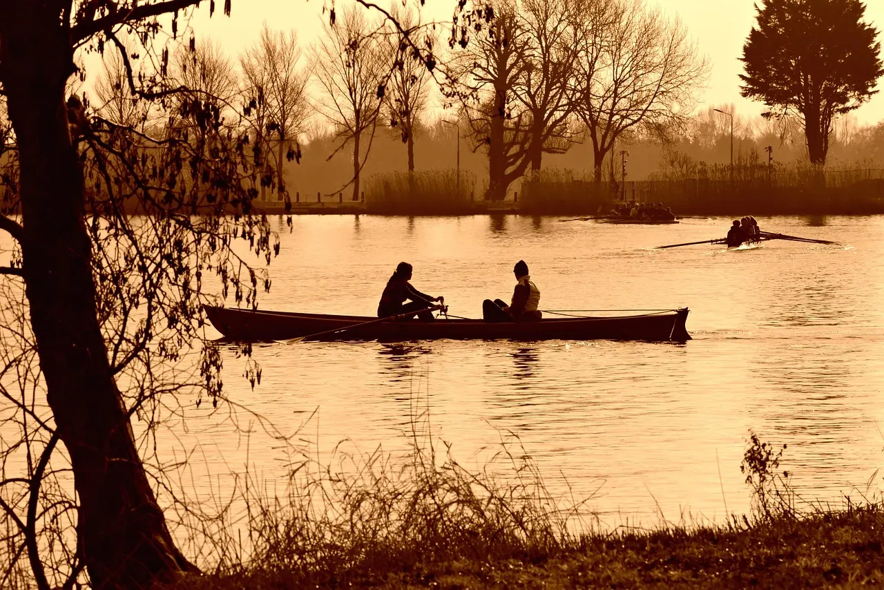 A rowing boat on calm water in low evening light, two rowers aboard