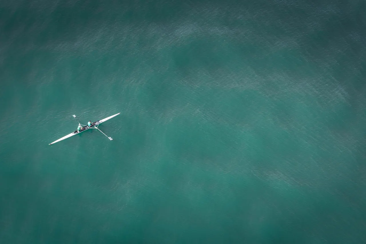 An aerial view of a rowing boat leaving a straight wake across open water