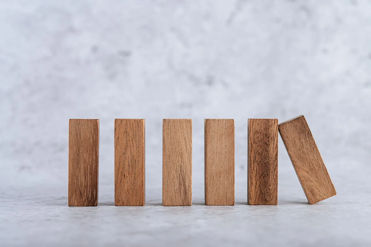 Wooden blocks standing in a row on a pale surface, the end one tipping