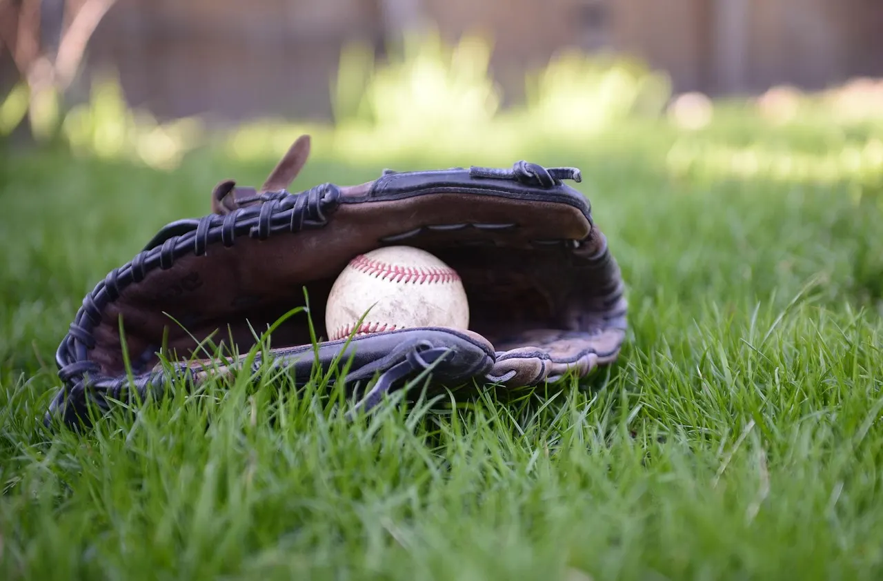 A worn leather baseball glove with a ball in its pocket, lying in grass