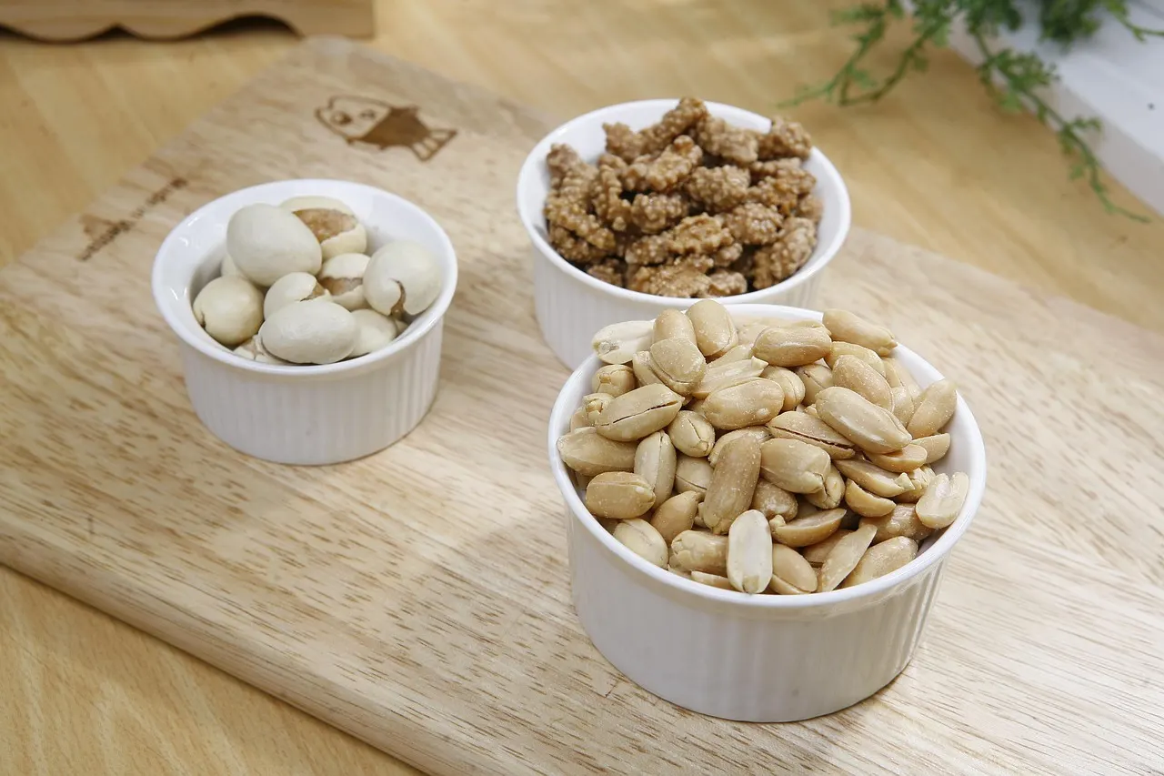 Small bowls of nuts sorted by kind on a light wooden table, seen from above