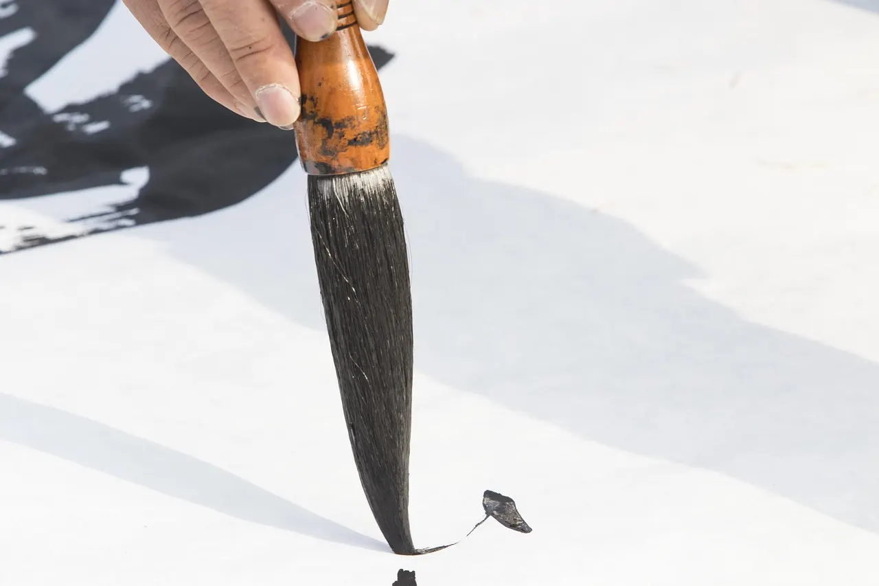 A calligraphy brush touching black ink to white paper