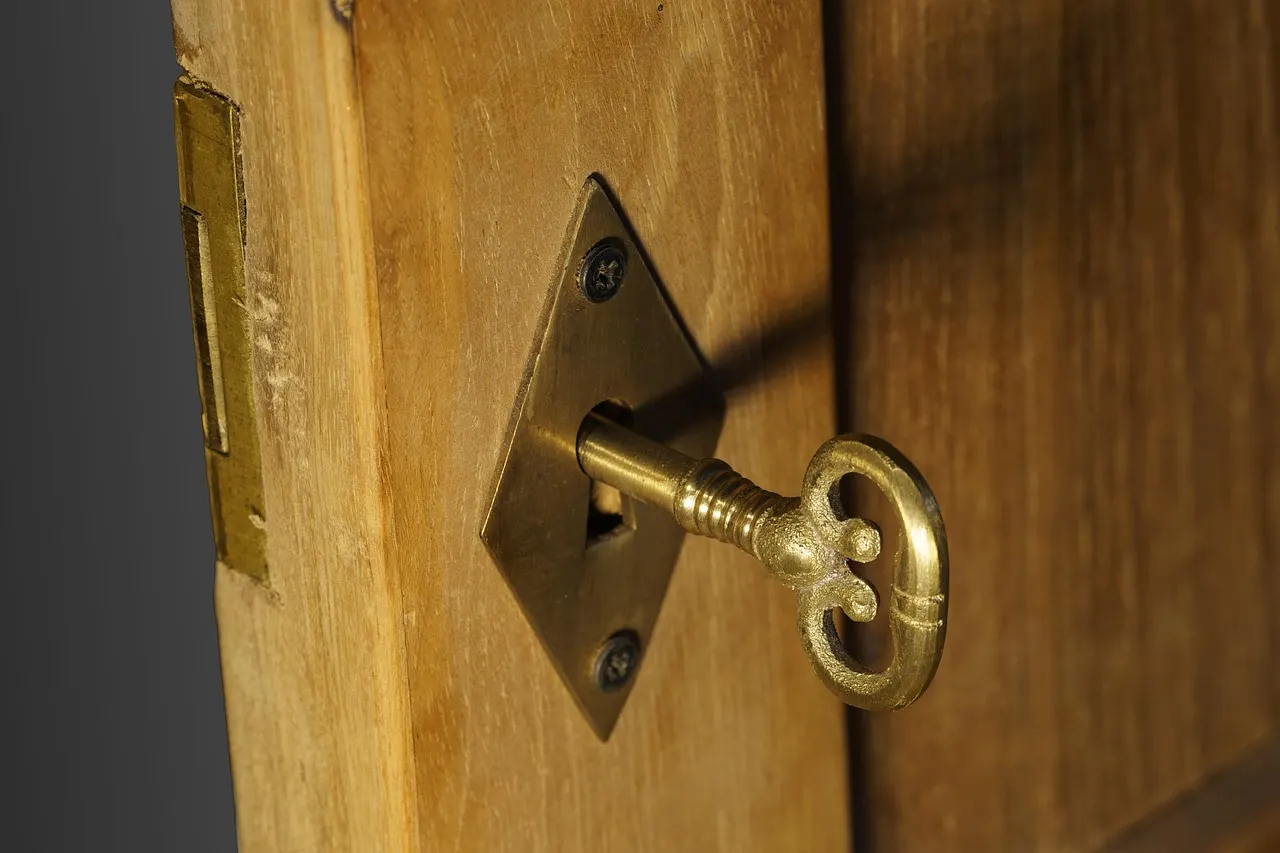 An ornate brass keyhole plate on a wooden door, a key resting in the lock